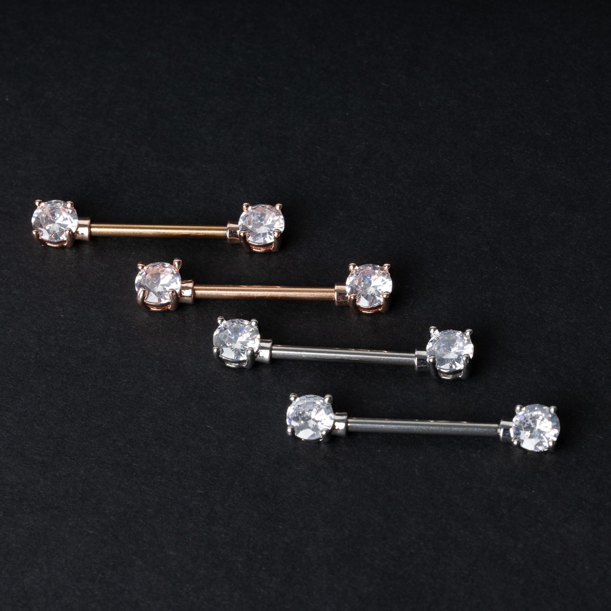 Crystal-studded barbells in gold, rose gold, and silver finishes, displayed on a dark background.