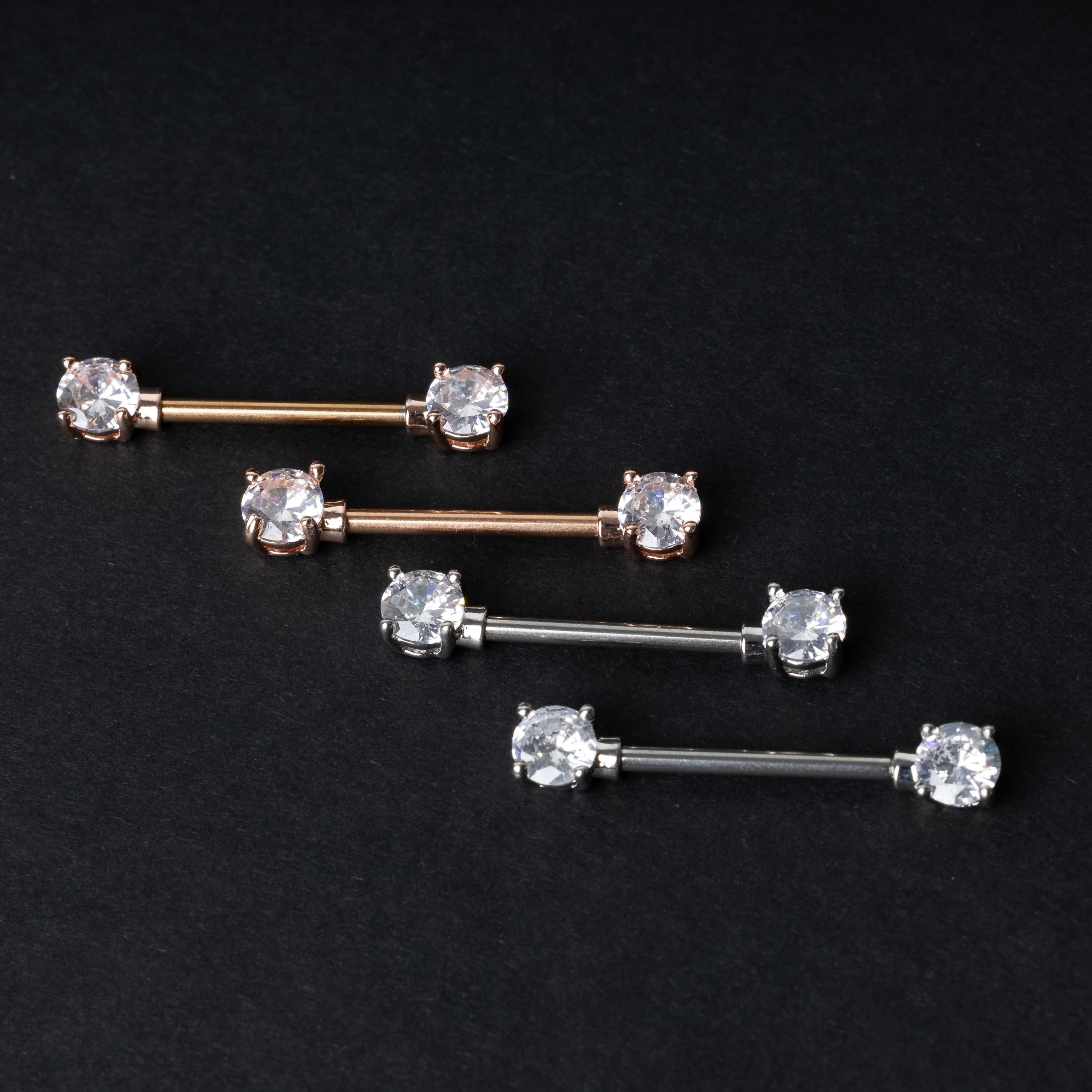 Crystal-studded barbells in gold, rose gold, and silver finishes, displayed on a dark background.