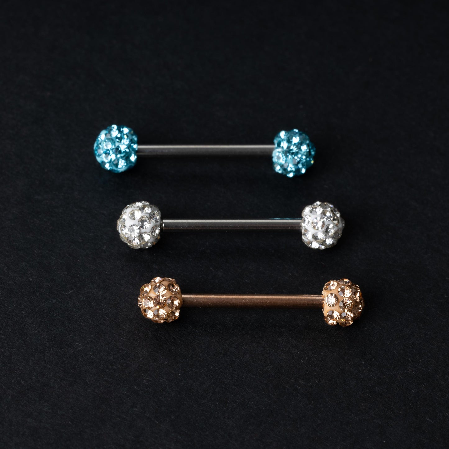 Barbells with textured crystal-encrusted ends in silver, gold, and icy blue finishes, displayed on a dark background.