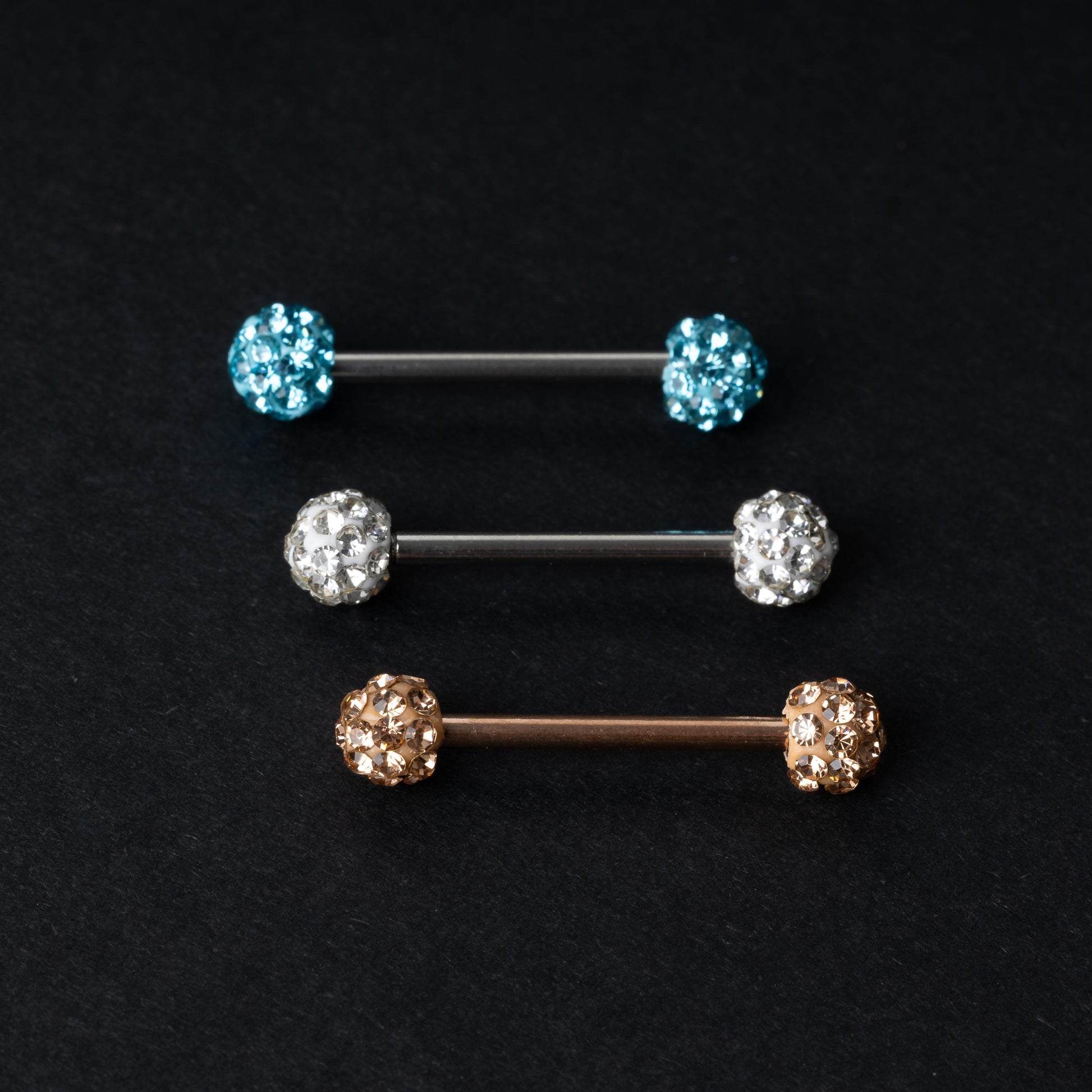 Barbells with textured crystal-encrusted ends in silver, gold, and icy blue finishes, displayed on a dark background.