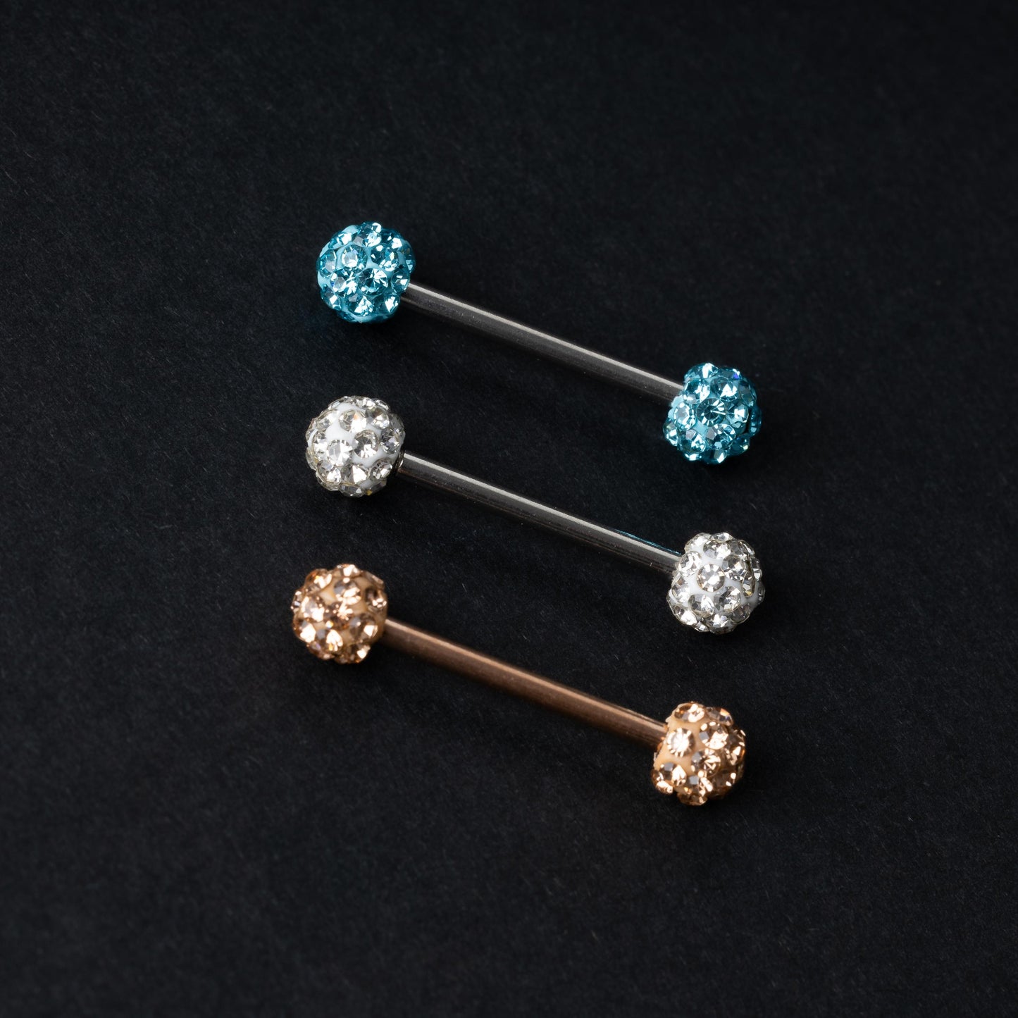 Barbells with textured crystal-encrusted ends in silver, gold, and icy blue finishes, displayed on a dark background.