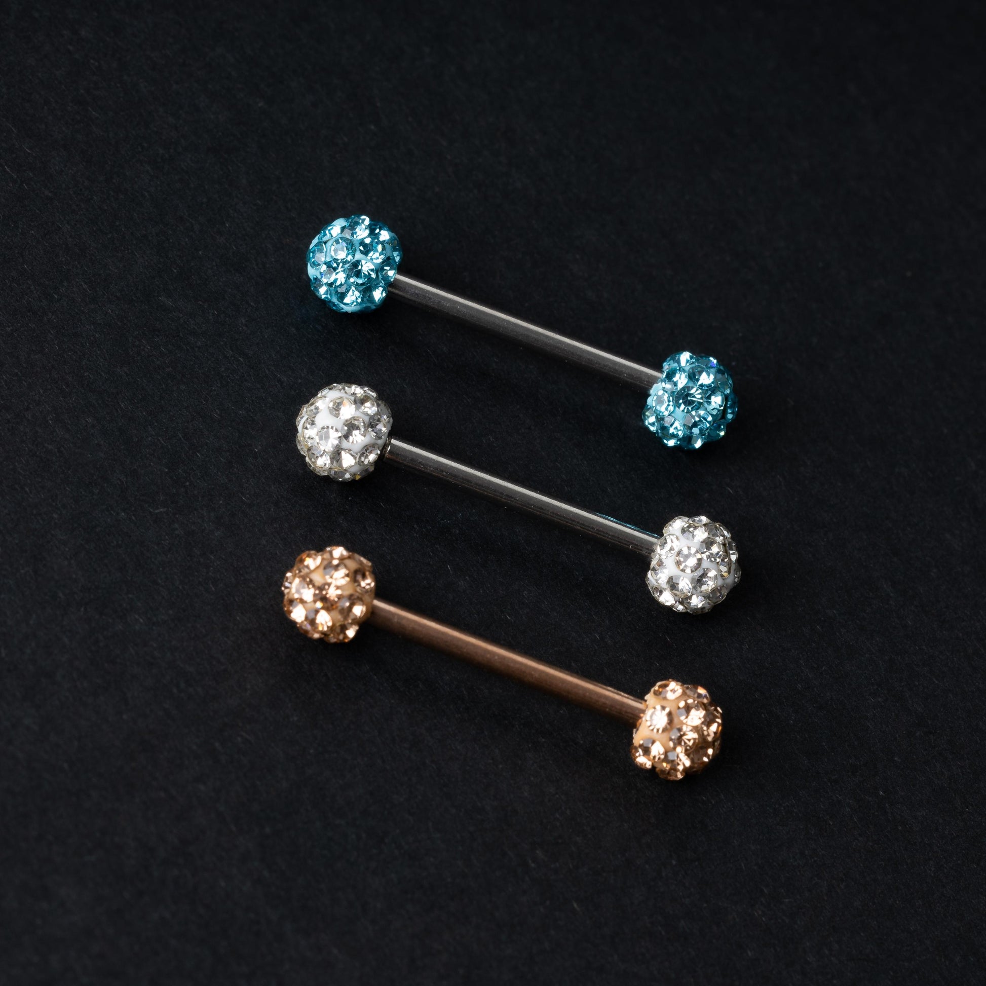 Barbells with textured crystal-encrusted ends in silver, gold, and icy blue finishes, displayed on a dark background.