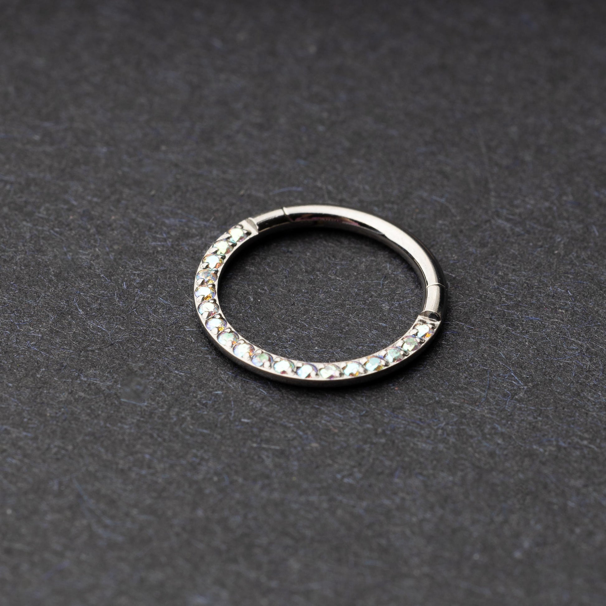 Titanium clicker ring with iridescent crystals, displayed on a dark background.