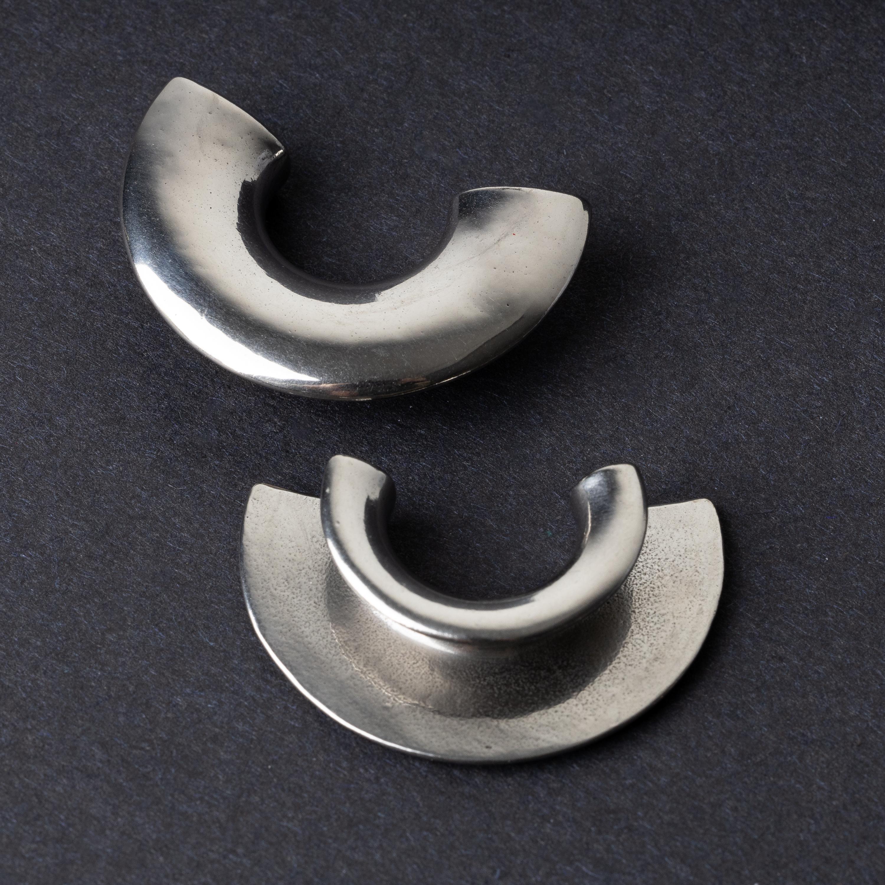 Close-up of two crescent-shaped stainless steel ear weights with a smooth, polished finish, displayed on a dark background.