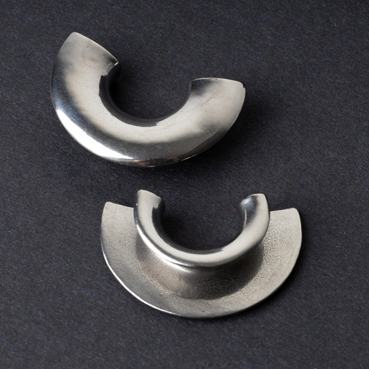 Close-up of two crescent-shaped stainless steel ear weights with a smooth, polished finish, displayed on a dark background.