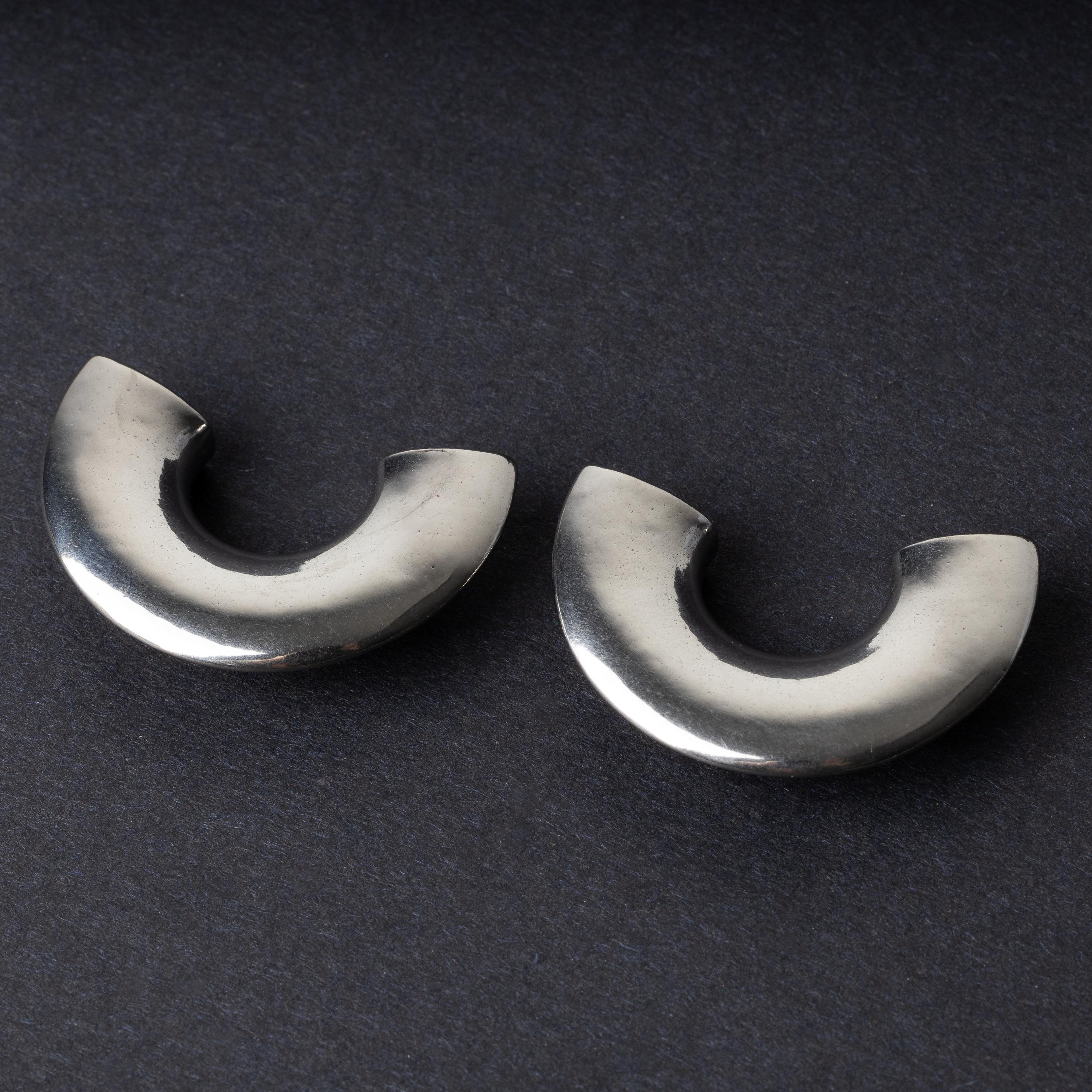 Close-up of two crescent-shaped stainless steel ear weights with a smooth, polished finish, displayed on a dark background.