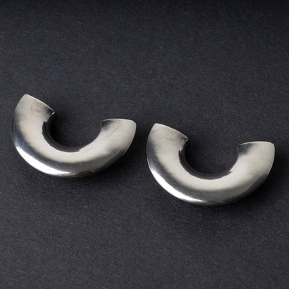 Close-up of two crescent-shaped stainless steel ear weights with a smooth, polished finish, displayed on a dark background.