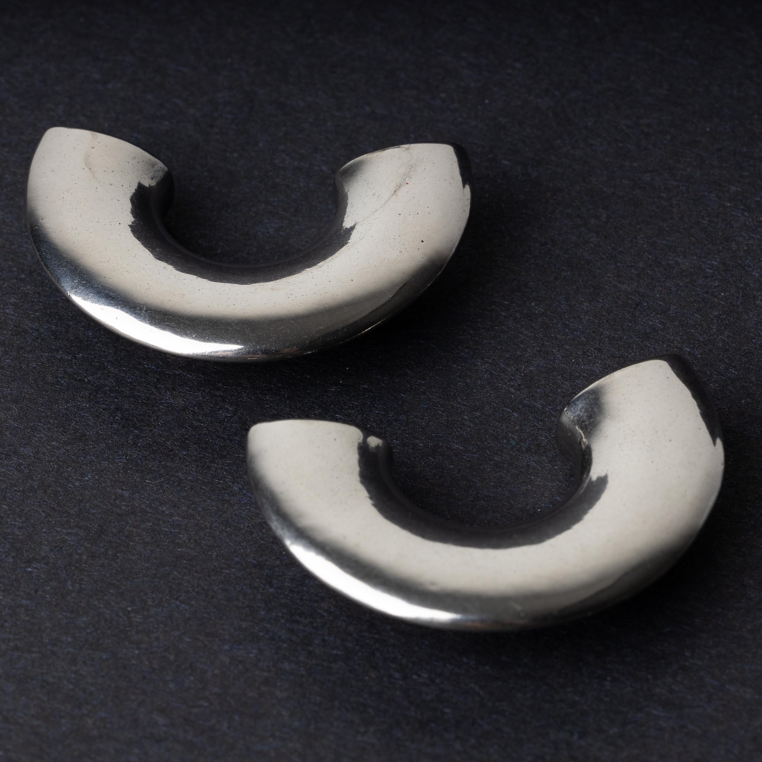 Close-up of two crescent-shaped stainless steel ear weights with a smooth, polished finish, displayed on a dark background.