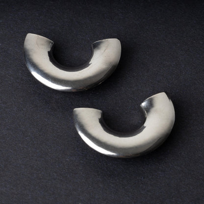 Close-up of two crescent-shaped stainless steel ear weights with a smooth, polished finish, displayed on a dark background.