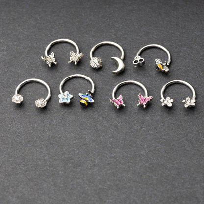 Silver horseshoe rings featuring various charms, including butterflies, bees, moons, and flowers, displayed on a dark background.