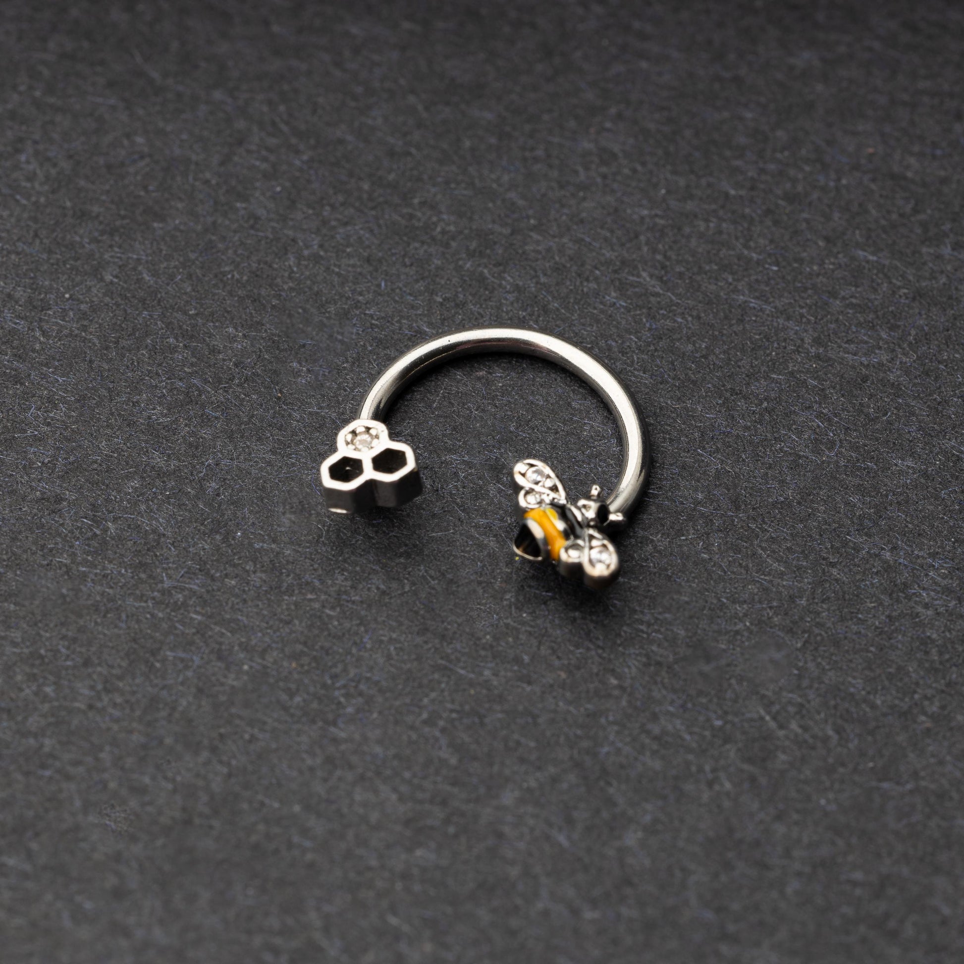 Horseshoe hoop featuring a bee charm, displayed on a dark background.