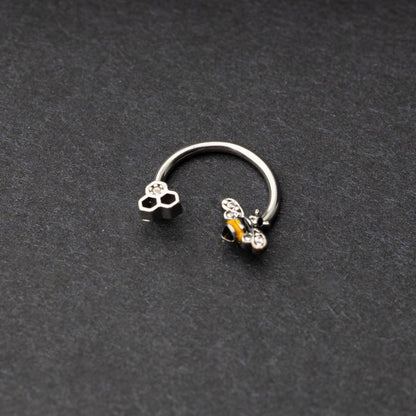 Horseshoe hoop featuring a bee charm, displayed on a dark background.
