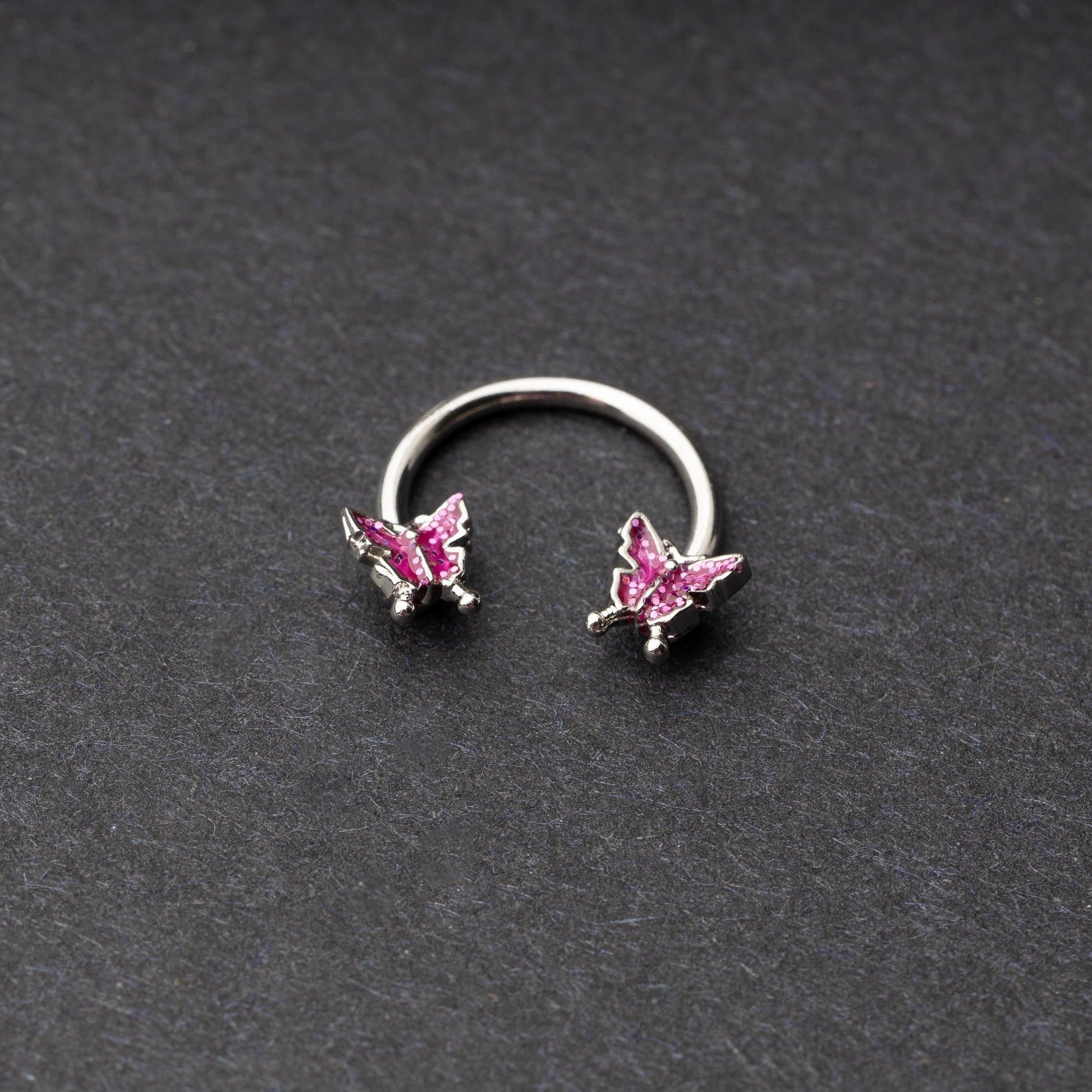 Horseshoe hoop featuring a butterfly charm, displayed on a dark background.