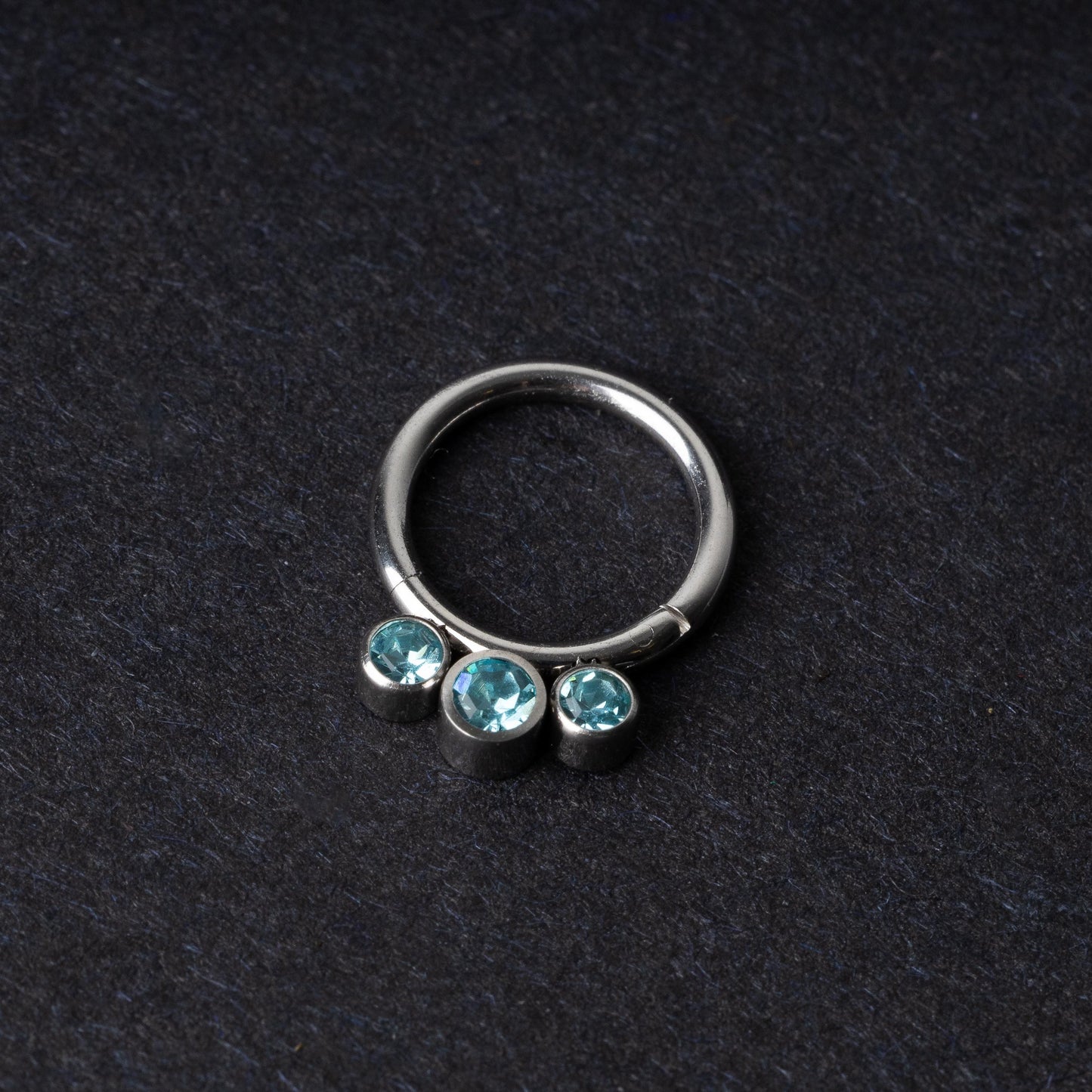 Titanium clicker ring with three aqua-blue gemstones, displayed on a dark background.