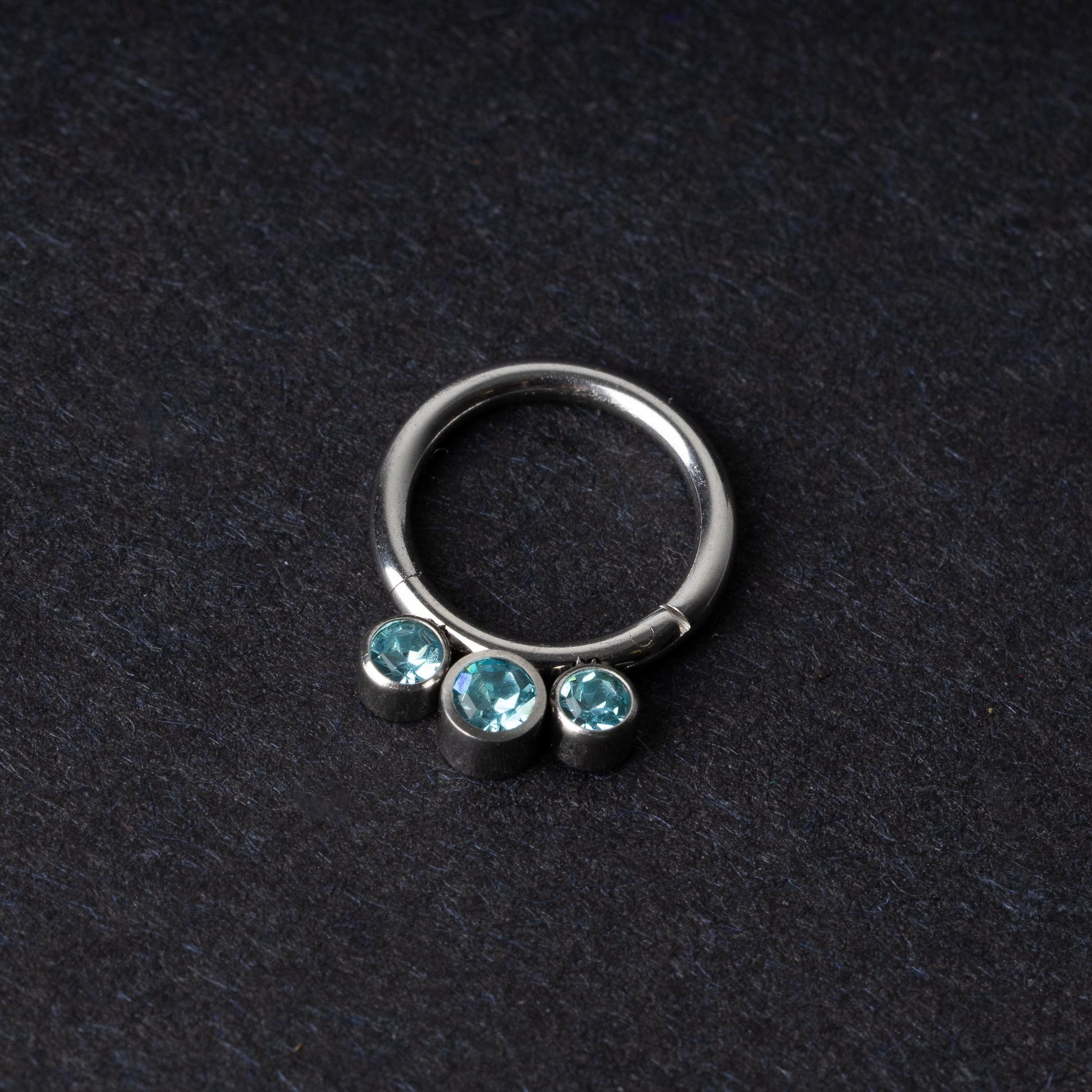 Titanium clicker ring with three aqua-blue gemstones, displayed on a dark background.
