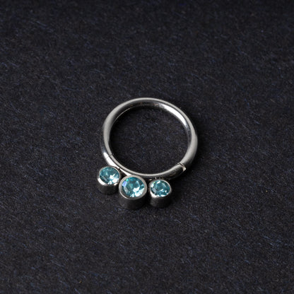 Titanium clicker ring with three aqua-blue gemstones, displayed on a dark background.