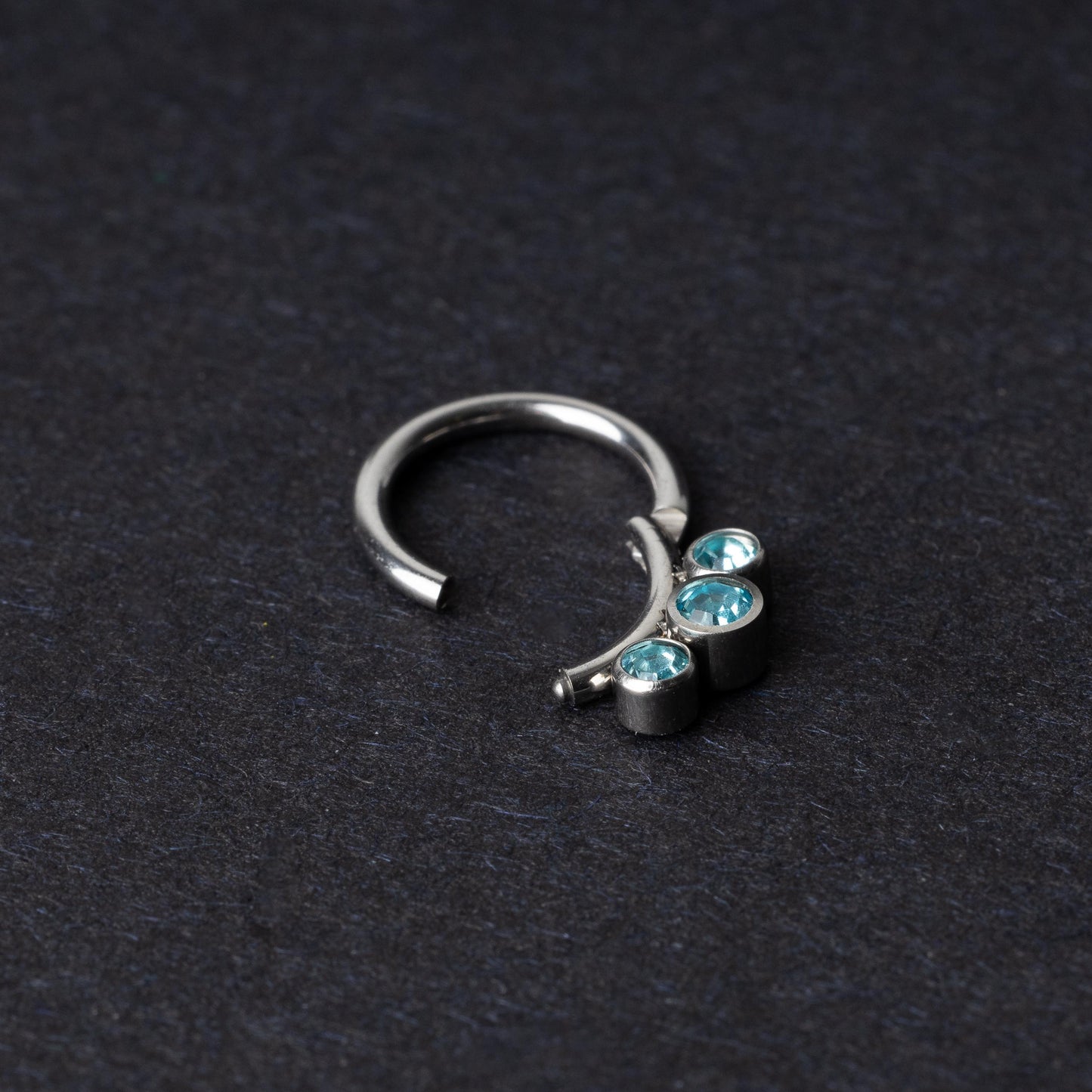 Titanium clicker ring with three aqua-blue gemstones, displayed on a dark background.