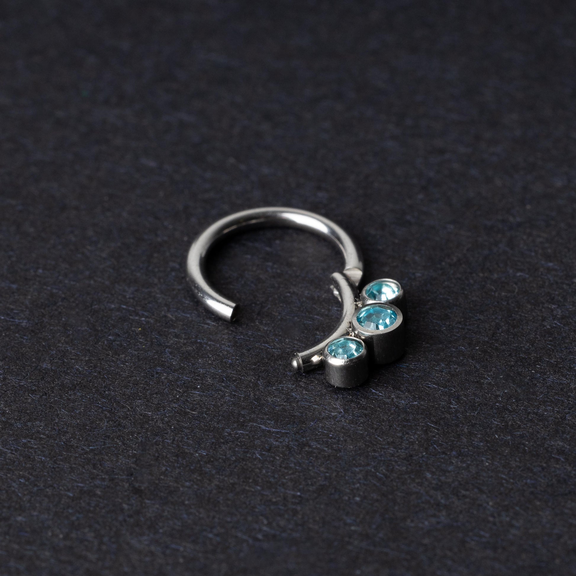 Titanium clicker ring with three aqua-blue gemstones, displayed on a dark background.