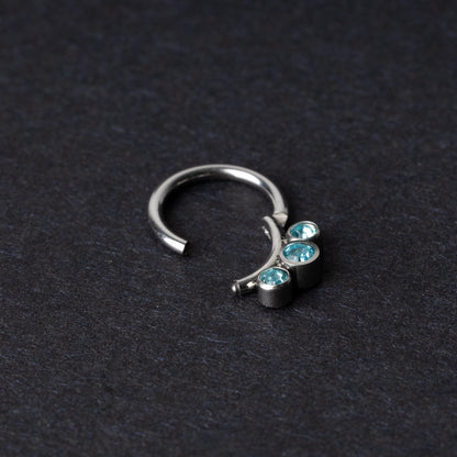 Titanium clicker ring with three aqua-blue gemstones, displayed on a dark background.