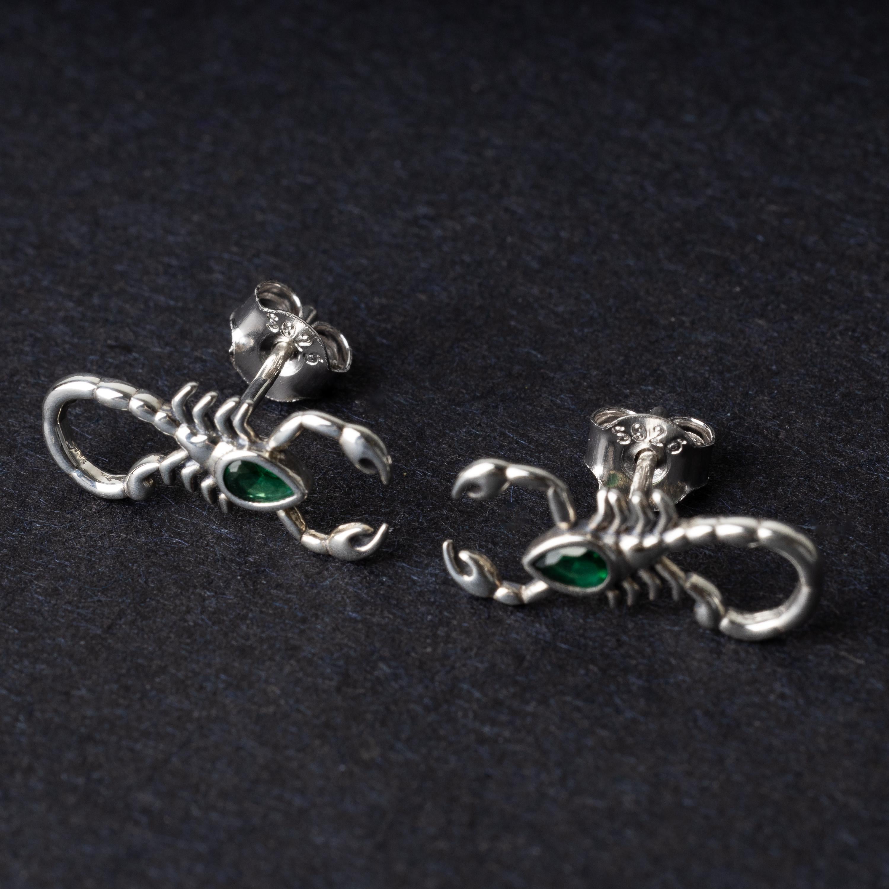 A pair of 925 sterling silver scorpion-shaped earrings with green gemstone accents as eyes, displayed on a dark background.
