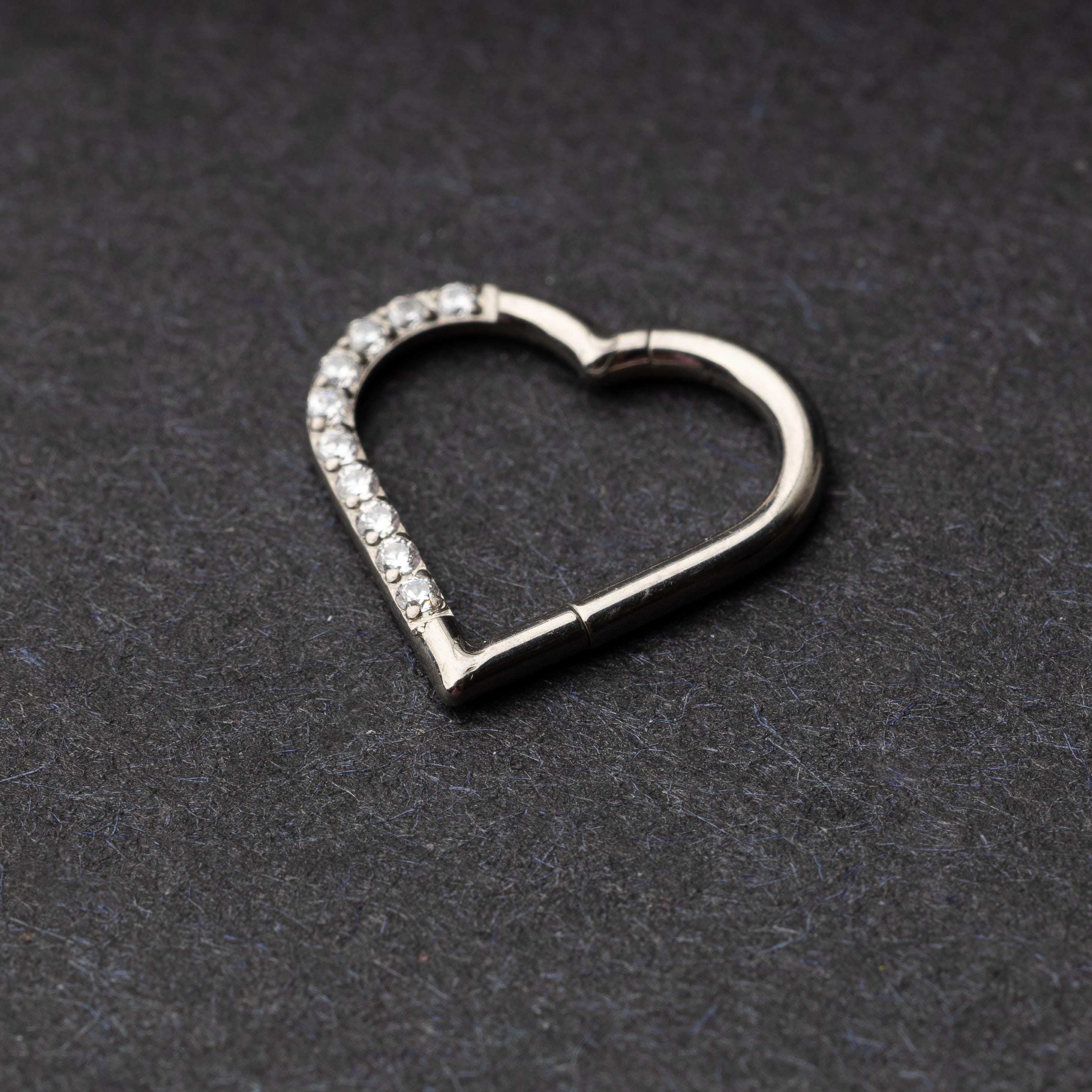 Heart-shaped daith clicker with crystal accents along one side, displayed on a dark textured background.