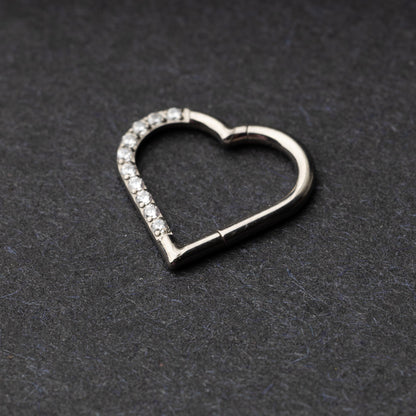 Heart-shaped daith clicker with crystal accents along one side, displayed on a dark textured background.