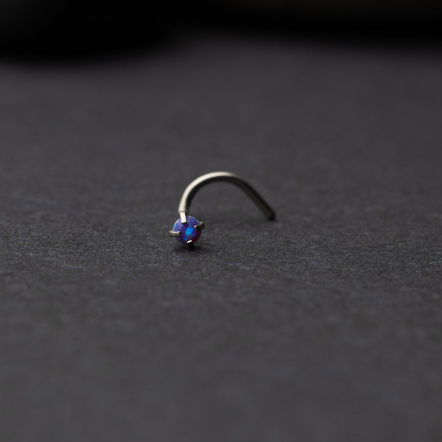Single opalescent nose screw with a prong setting, displayed on a dark background.
