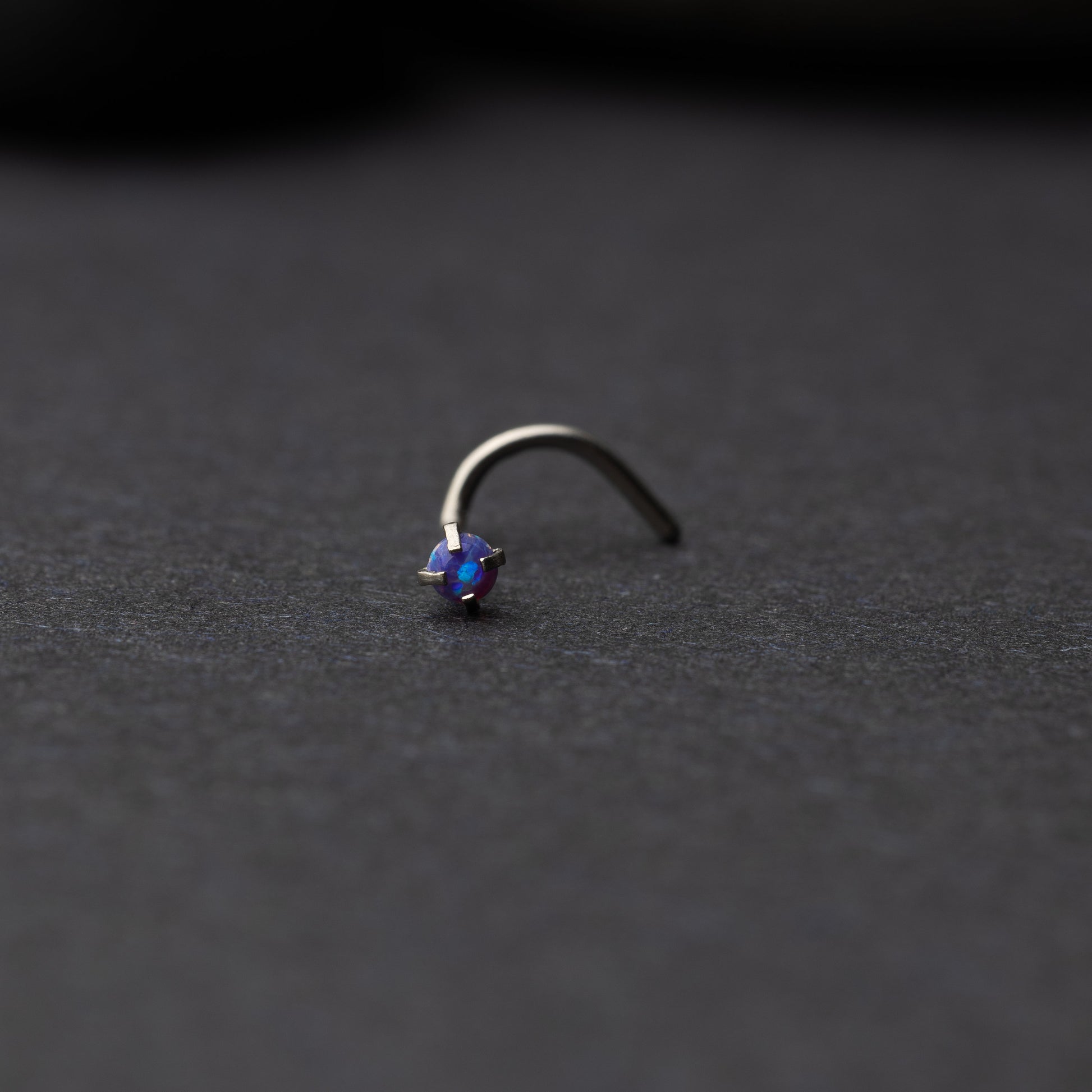 Single opalescent nose screw with a prong setting, displayed on a dark background.