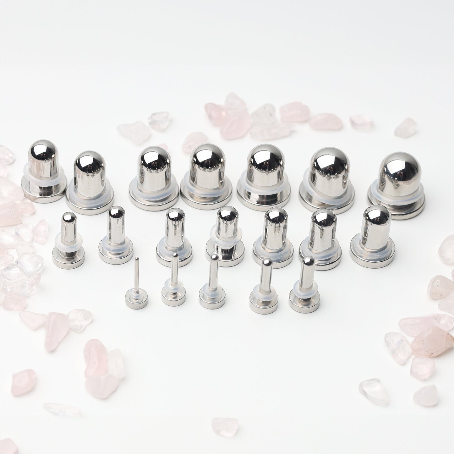 A complete dead stretching kit with polished stainless steel plugs and tunnels in multiple sizes, displayed on a white background with scattered rose quartz accents.