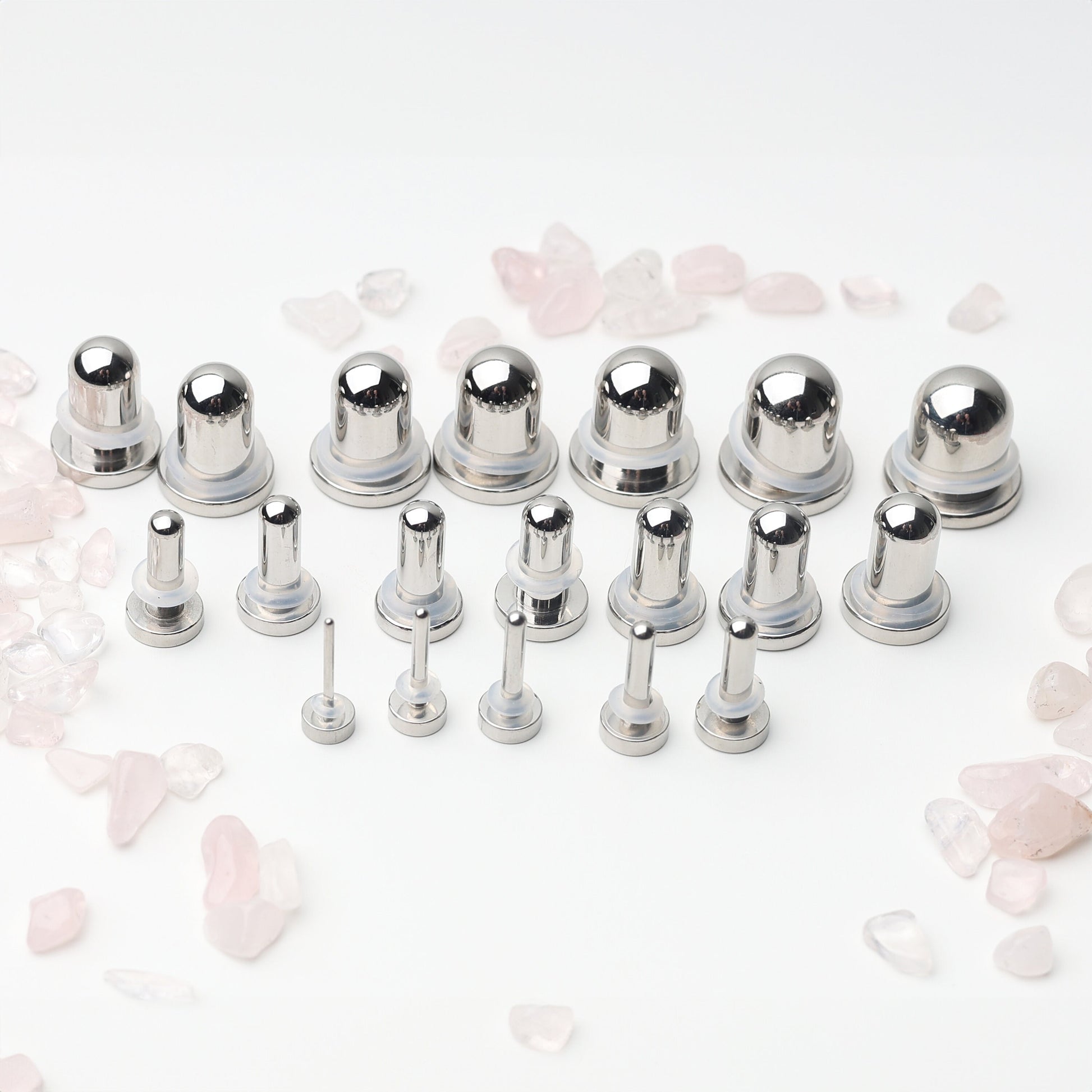 A complete dead stretching kit with polished stainless steel plugs and tunnels in multiple sizes, displayed on a white background with scattered rose quartz accents.