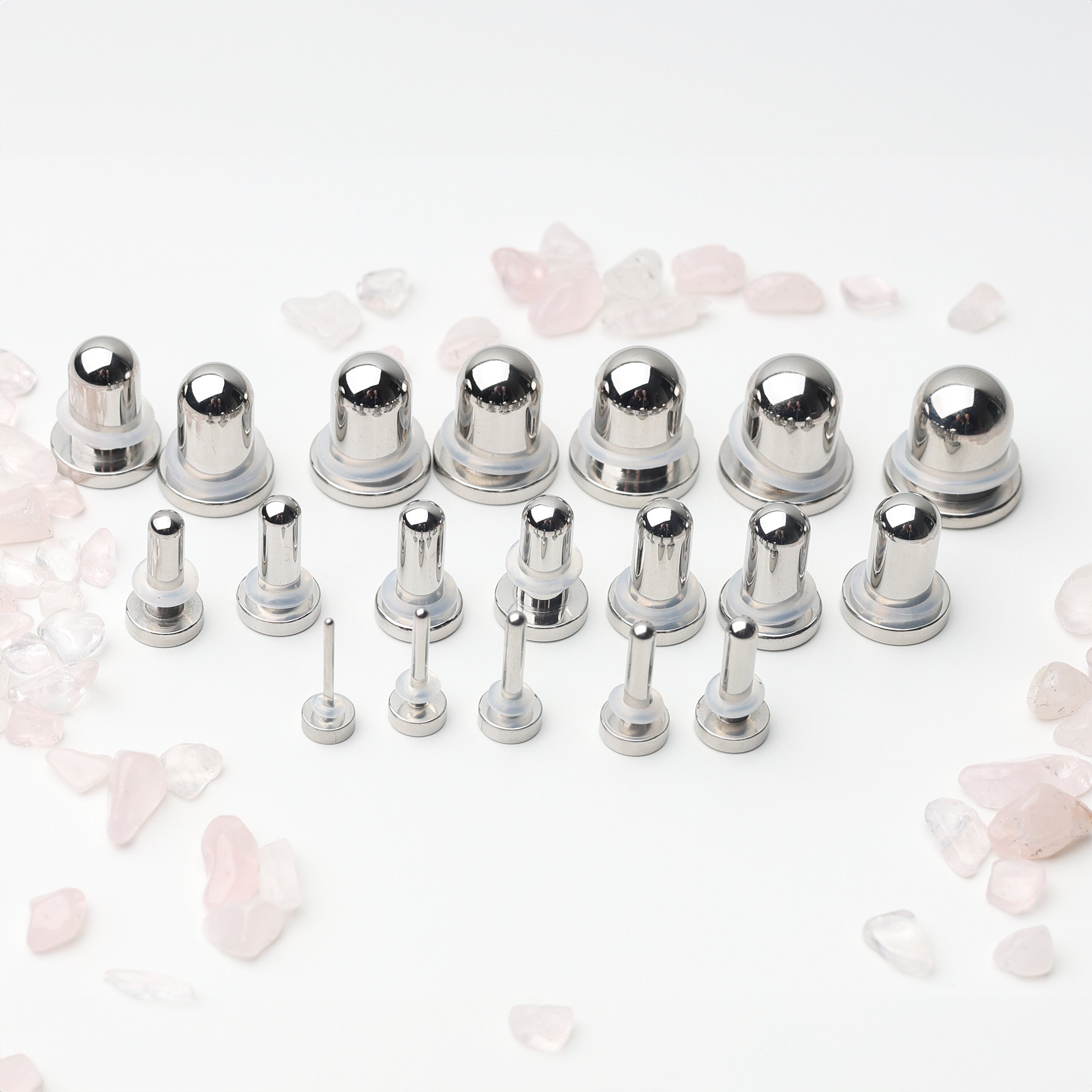 A complete dead stretching kit with polished stainless steel plugs and tunnels in multiple sizes, displayed on a white background with scattered rose quartz accents.