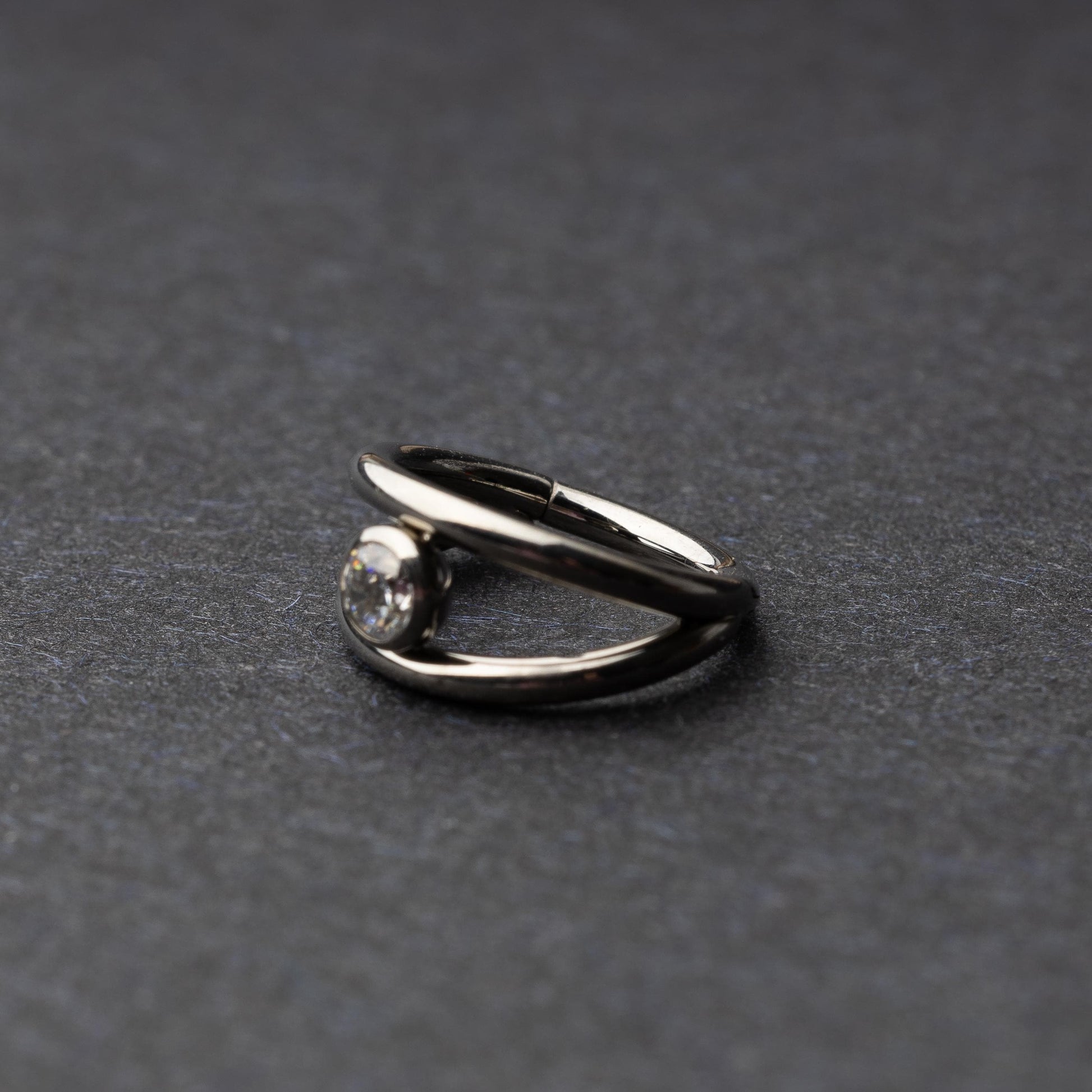 Titanium double-layered clicker with a single cubic zirconia centerpiece, displayed on a dark background.