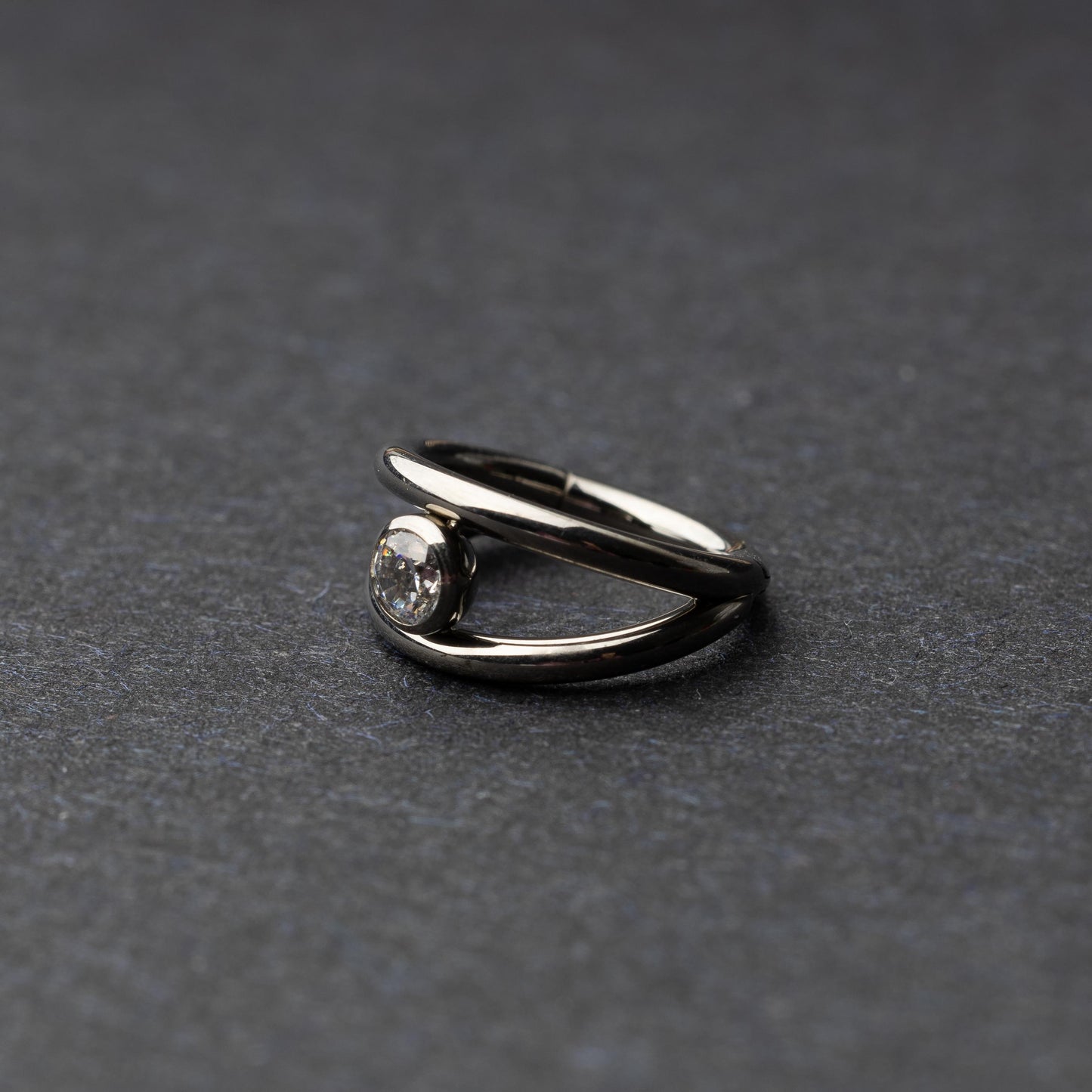 Titanium double-layered clicker with a single cubic zirconia centerpiece, displayed on a dark background.