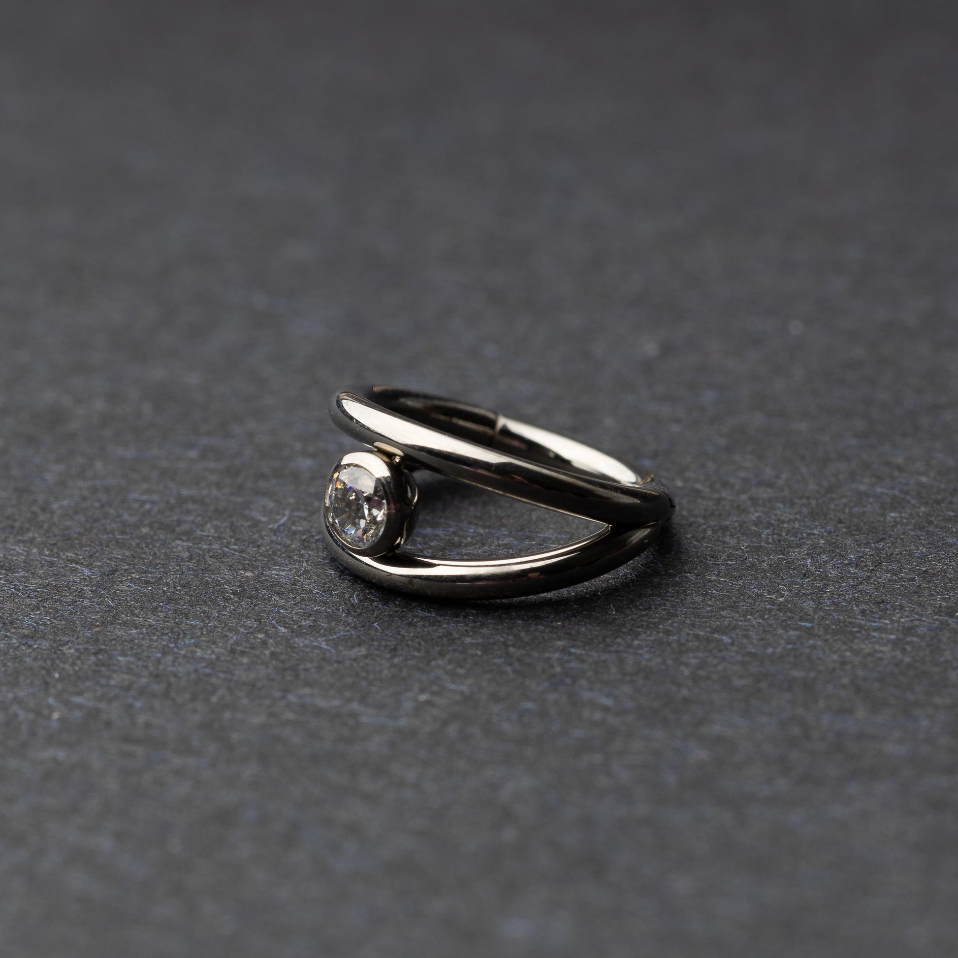 Titanium double-layered clicker with a single cubic zirconia centerpiece, displayed on a dark background.