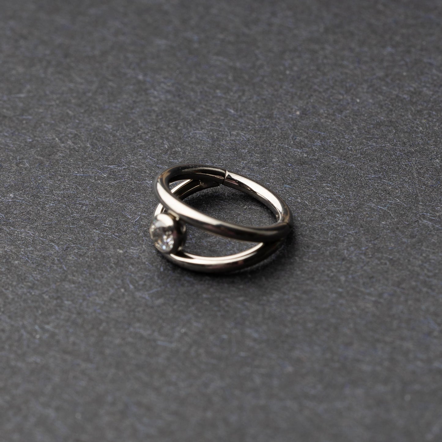 Titanium double-layered clicker with a single cubic zirconia centerpiece, displayed on a dark background.