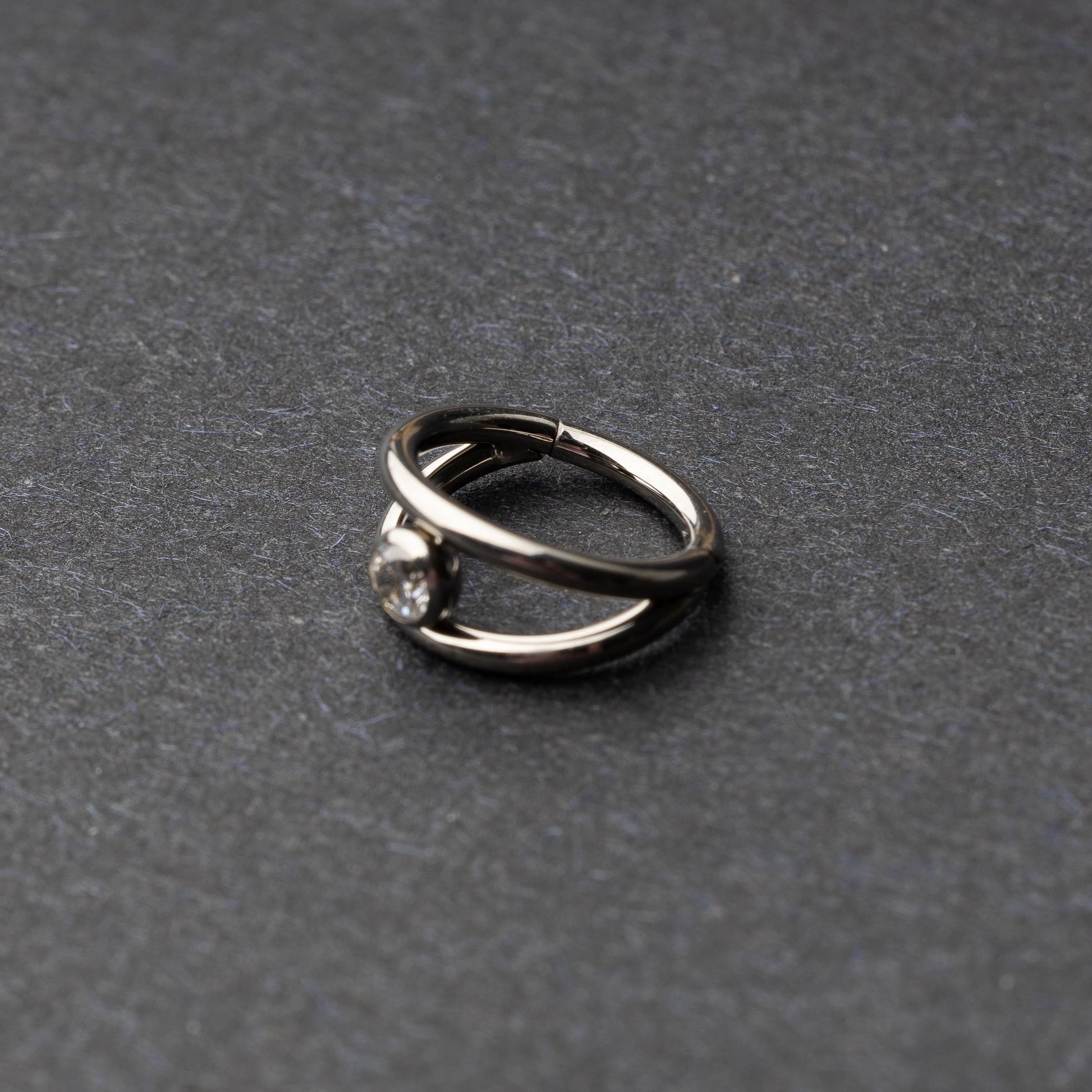Titanium double-layered clicker with a single cubic zirconia centerpiece, displayed on a dark background.