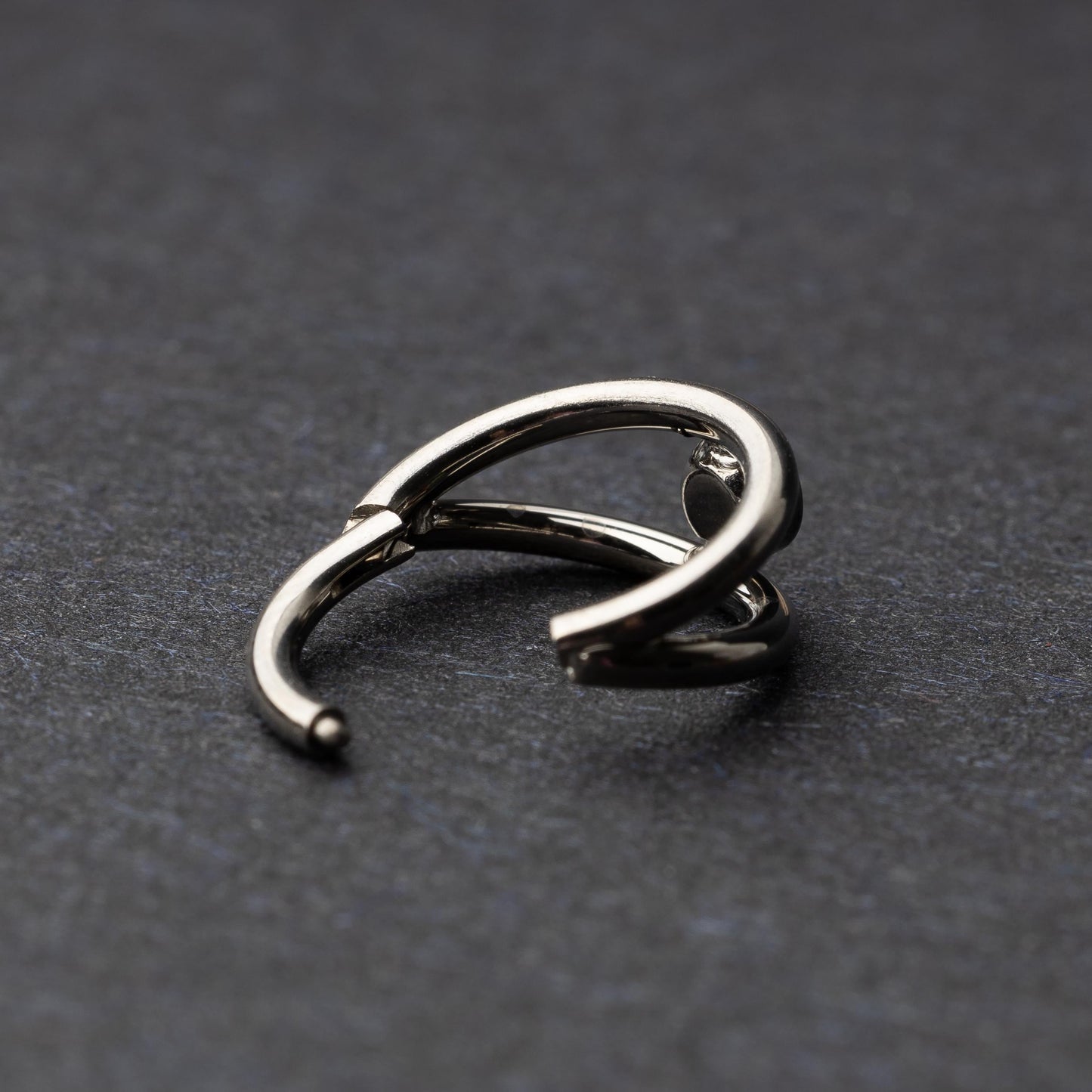 Titanium double-layered clicker with a single cubic zirconia centerpiece, displayed on a dark background.