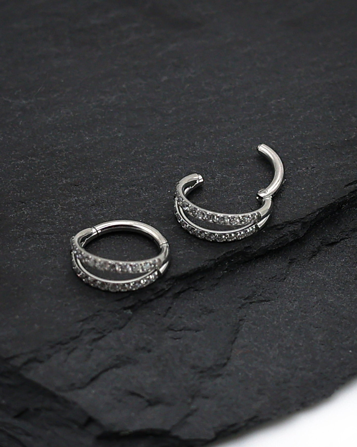Titanium double-row clickers with cubic zirconia accents, displayed on a textured dark background.