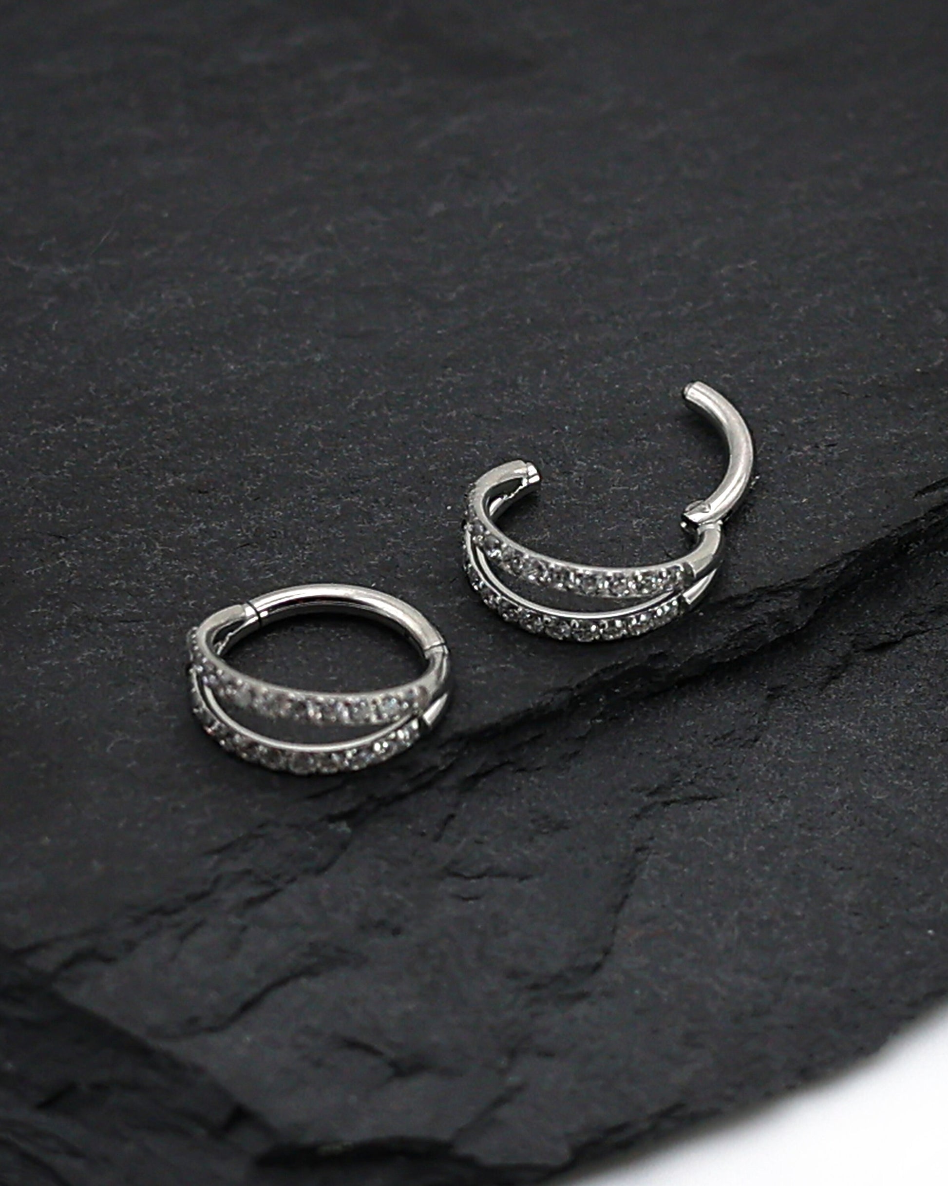Titanium double-row clickers with cubic zirconia accents, displayed on a textured dark background.