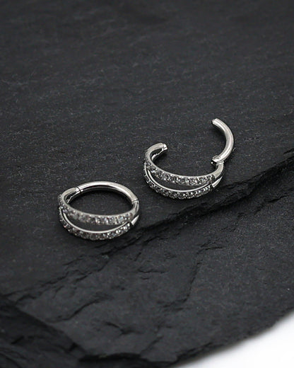 Titanium double-row clickers with cubic zirconia accents, displayed on a textured dark background.