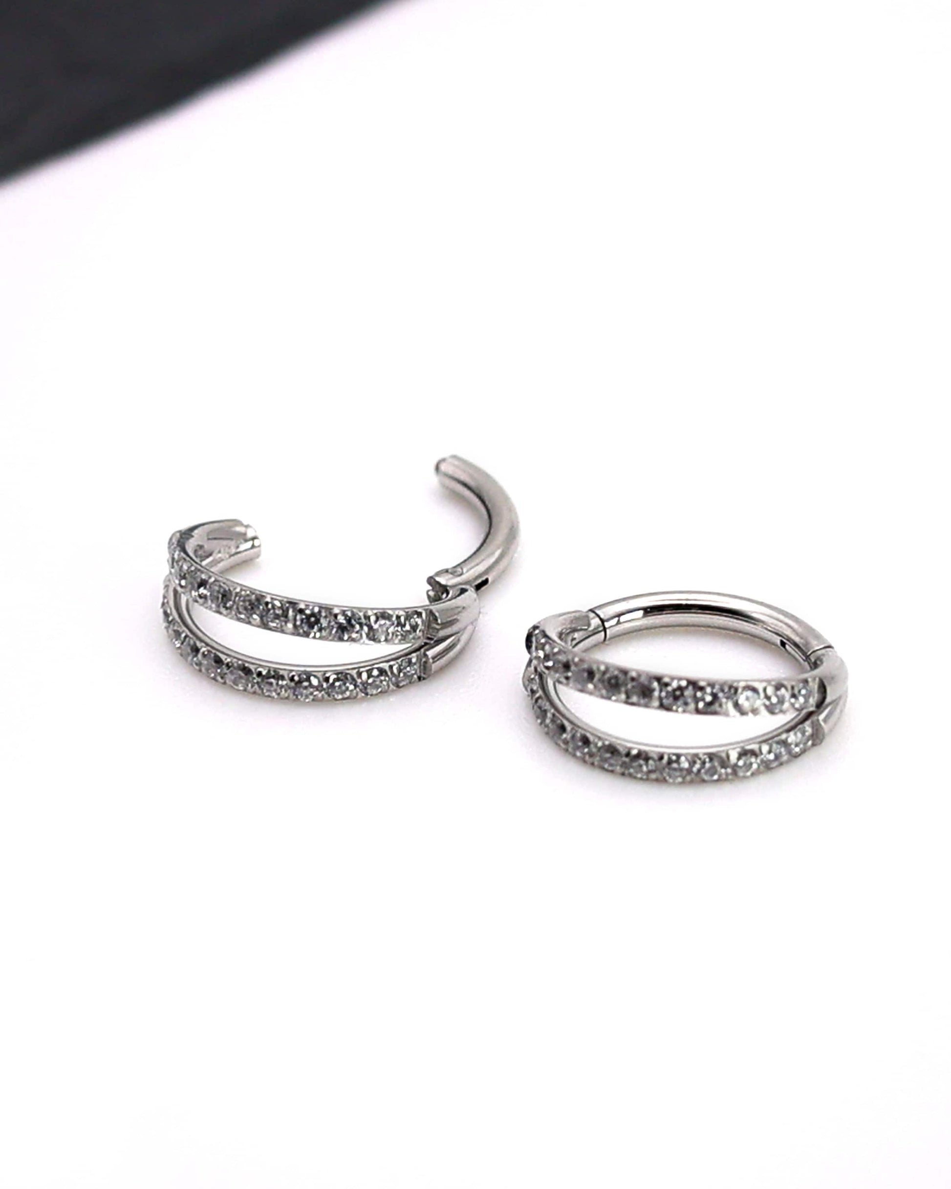 Titanium double-row clickers with cubic zirconia accents, displayed on a textured white background.