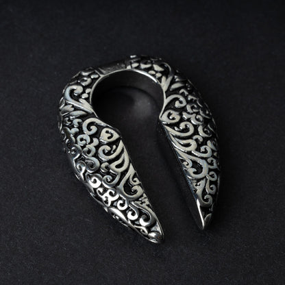 A pair of split ear weights in polished silver with detailed filigree patterns, displayed on a dark background.

