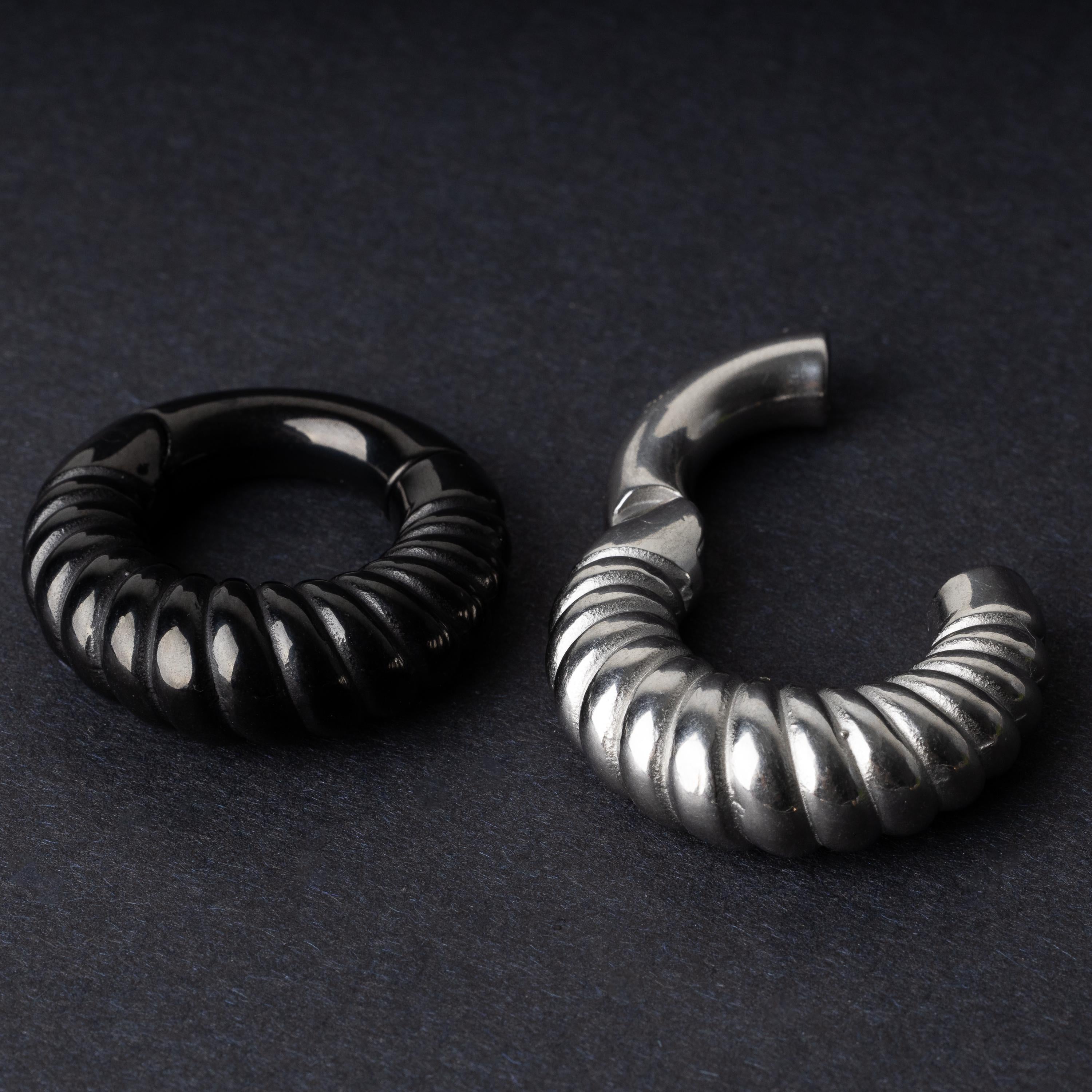 Two textured hoop rings with a ridged design, one in black and one in silver, displayed side by side on a dark background.