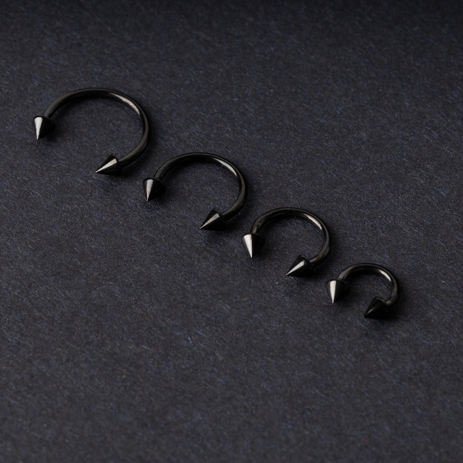 Four G23 titanium black horseshoe rings with spiked ends in varying sizes, displayed on a dark background showcasing their polished finish.