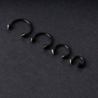Four G23 titanium black horseshoe rings with spiked ends in varying sizes, displayed on a dark background showcasing their polished finish.