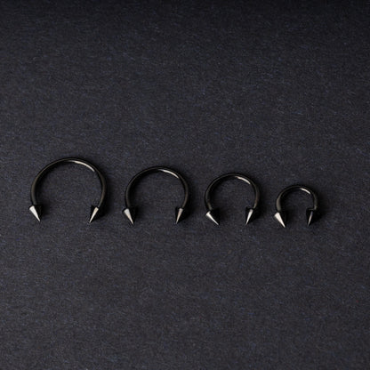 Four G23 titanium black horseshoe rings with spiked ends in varying sizes, displayed on a dark background showcasing their polished finish.