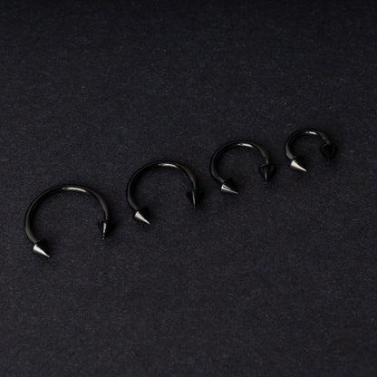 Four G23 titanium black horseshoe rings with spiked ends in varying sizes, displayed on a dark background showcasing their polished finish.