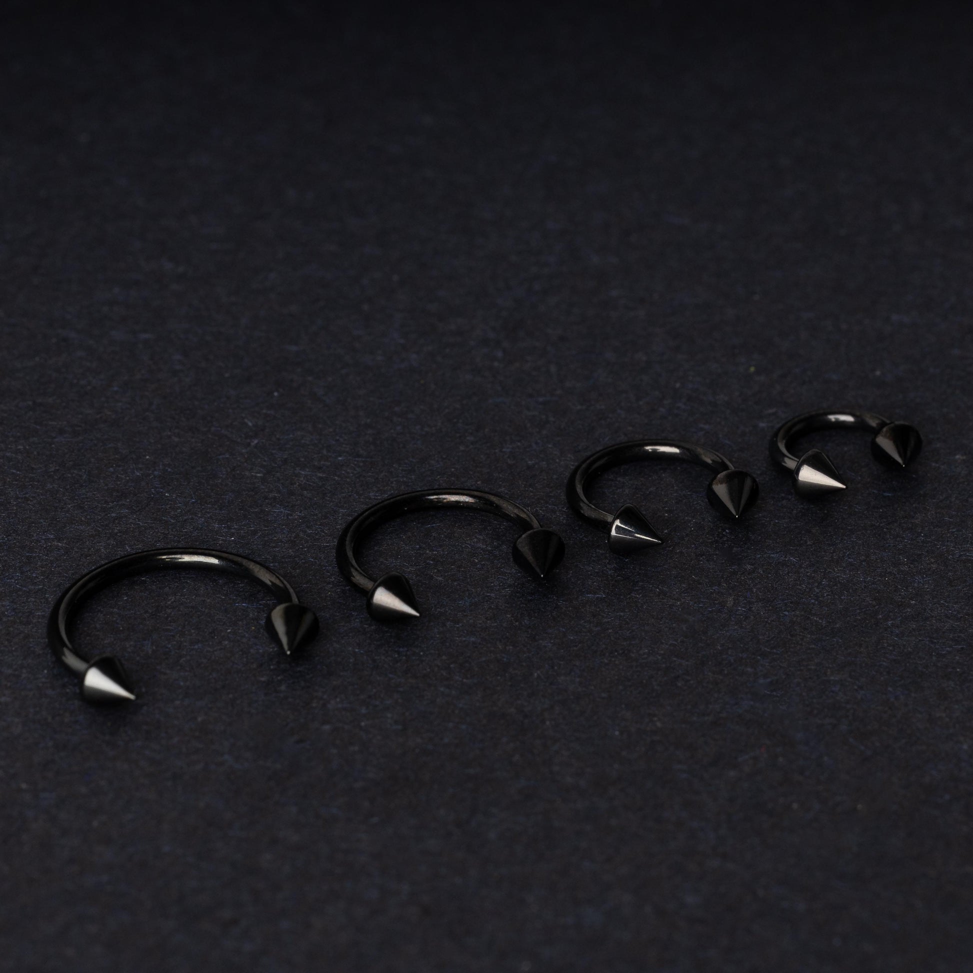 Four G23 titanium black horseshoe rings with spiked ends in varying sizes, displayed on a dark background showcasing their polished finish.