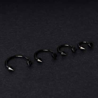 Four G23 titanium black horseshoe rings with spiked ends in varying sizes, displayed on a dark background showcasing their polished finish.