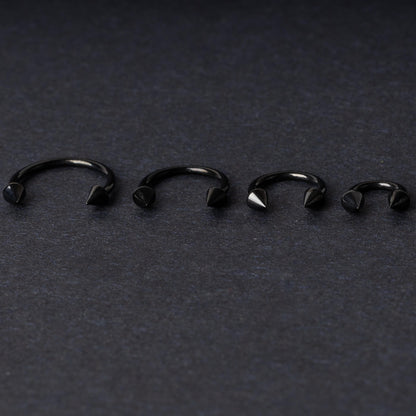 Four G23 titanium black horseshoe rings with spiked ends in varying sizes, displayed on a dark background showcasing their polished finish.